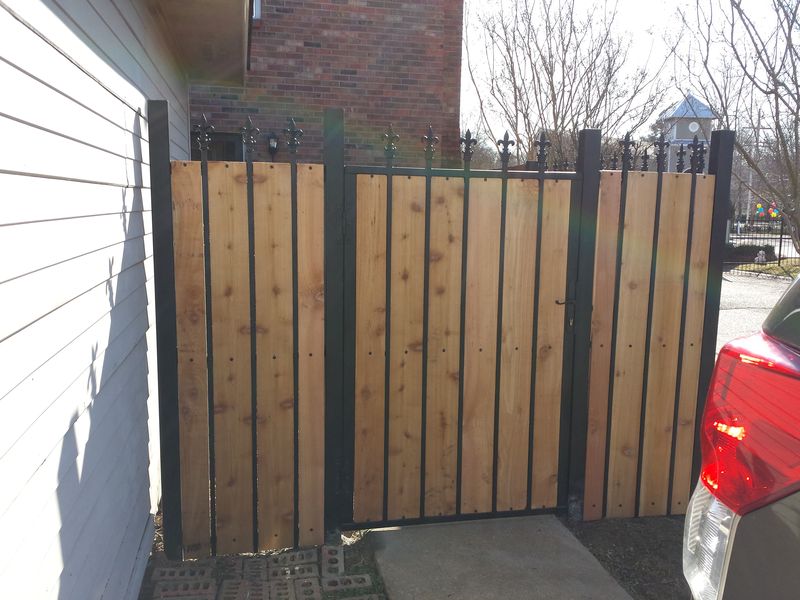 Custom privacy fence and gate with vertical cedar boards in a black steel frame topped with fleur-de-lis finials