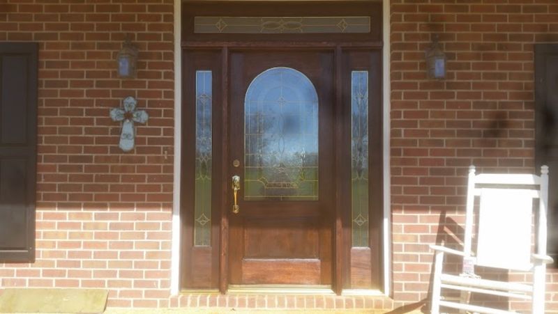 Refinished dark-stained wood entry door with an arched leaded-glass panel, leaded-glass sidelights and a transom on a brick home