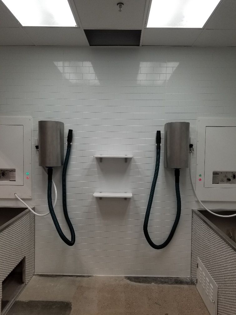 Finished grooming room with a white subway tile wall, two wall-mounted pet dryers and shelves