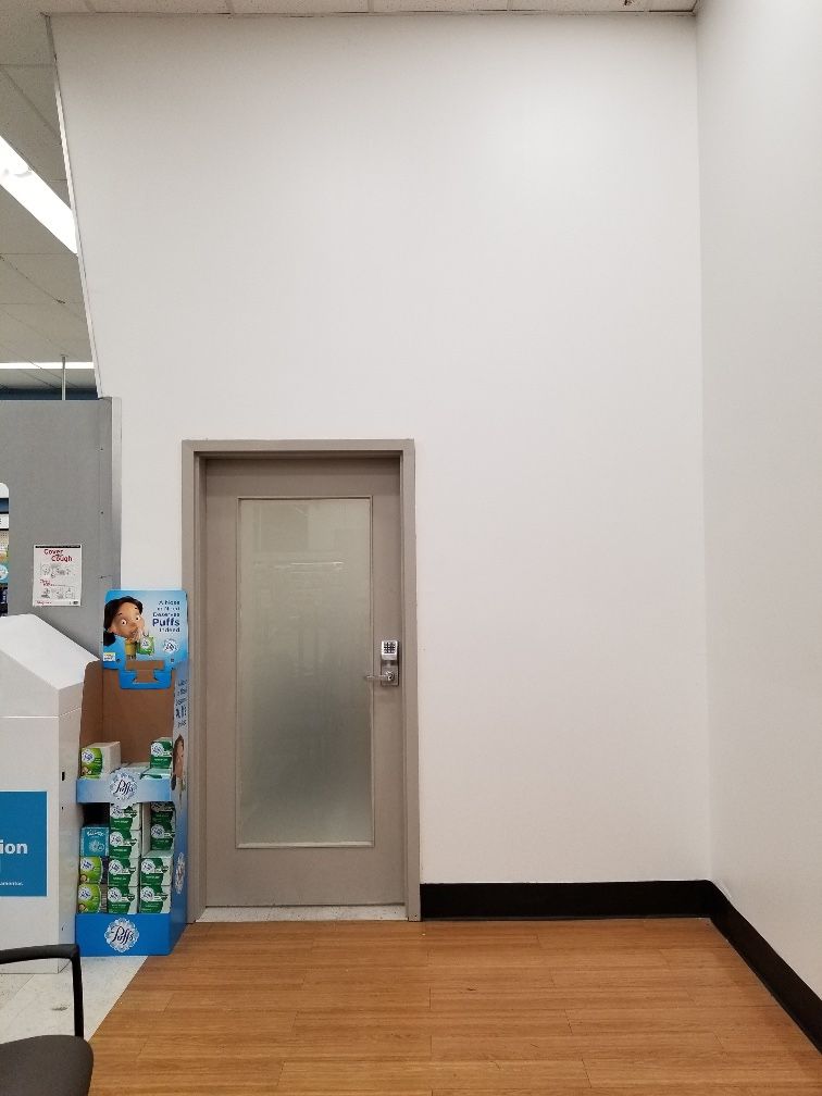 Gray metal door with a frosted glass panel and a keypad lock in a freshly painted white wall inside a pharmacy store