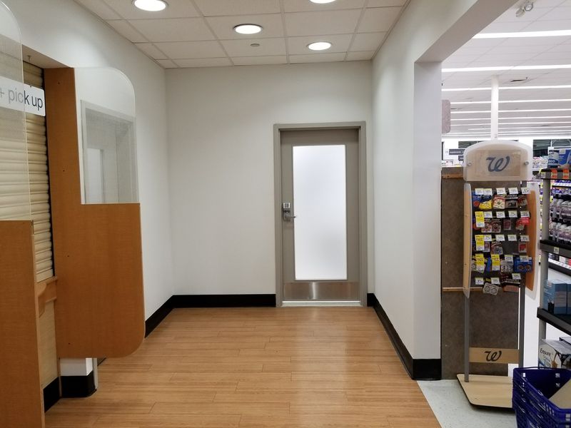 Store hallway ending at a new door with a frosted glass panel and a metal kick plate
